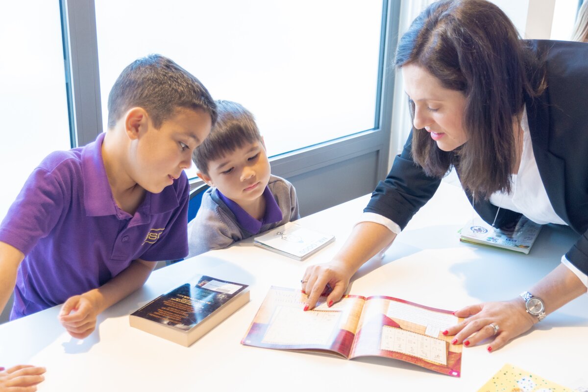 teacher pointing a book to two students
